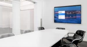 Conference room featuring a large Zoom display on the wall, showcasing meeting details and a sleek table with black chairs.